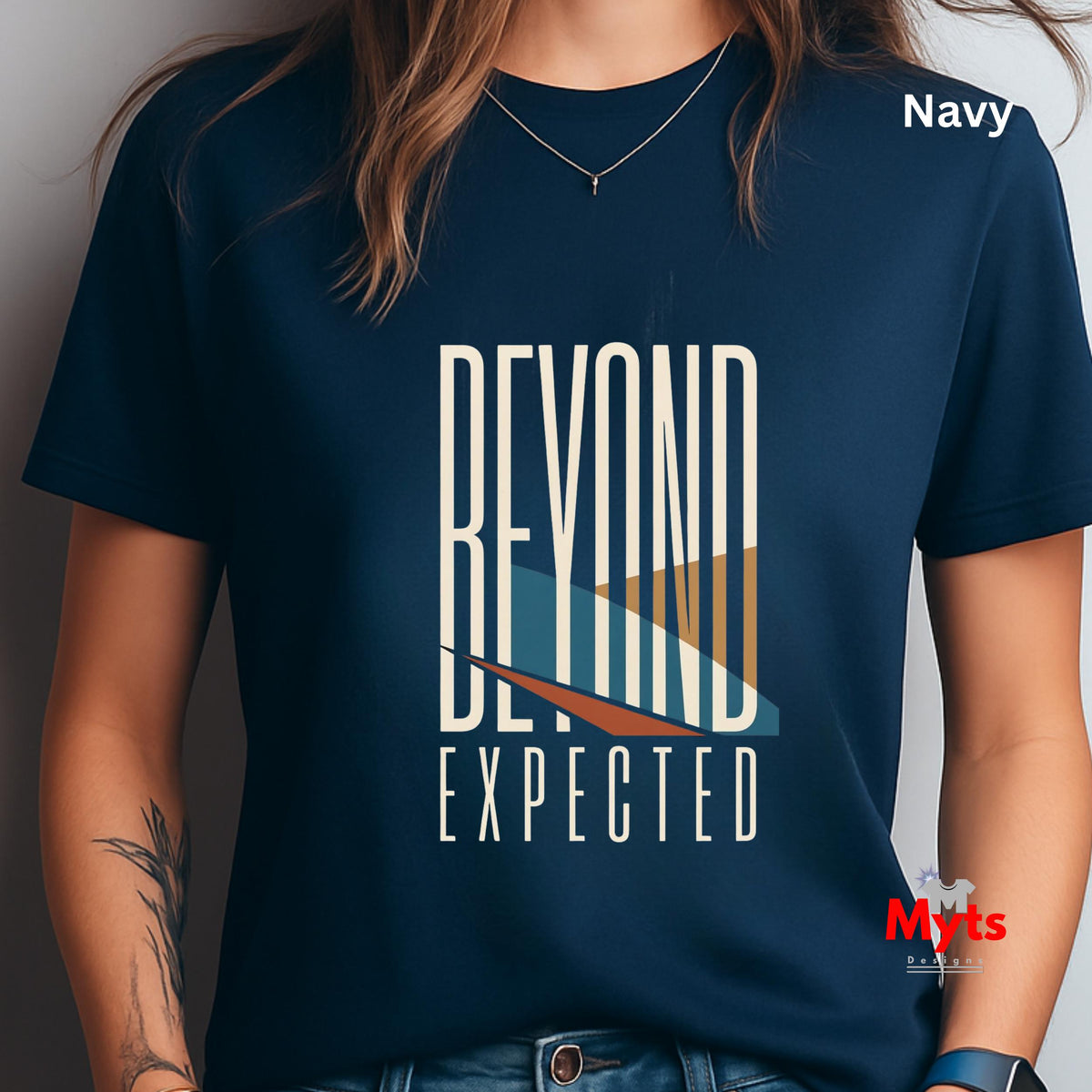 A person wearing a navy blue graphic T-shirt with the words 'BEYOND EXPECTED' in large white letters and a stylized wave design in white, teal, and orange. The shirt is shown on a model against a plain indoor background, with 'Navy' text in the upper right and a small 'Myts' watermark/logo in the lower right.