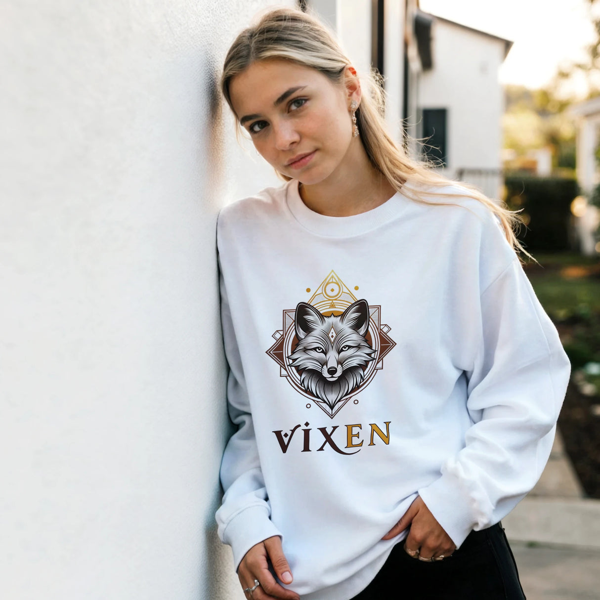 Woman wearing a white sweatshirt with a fox design and 'Vixen' text, standing against a wall.