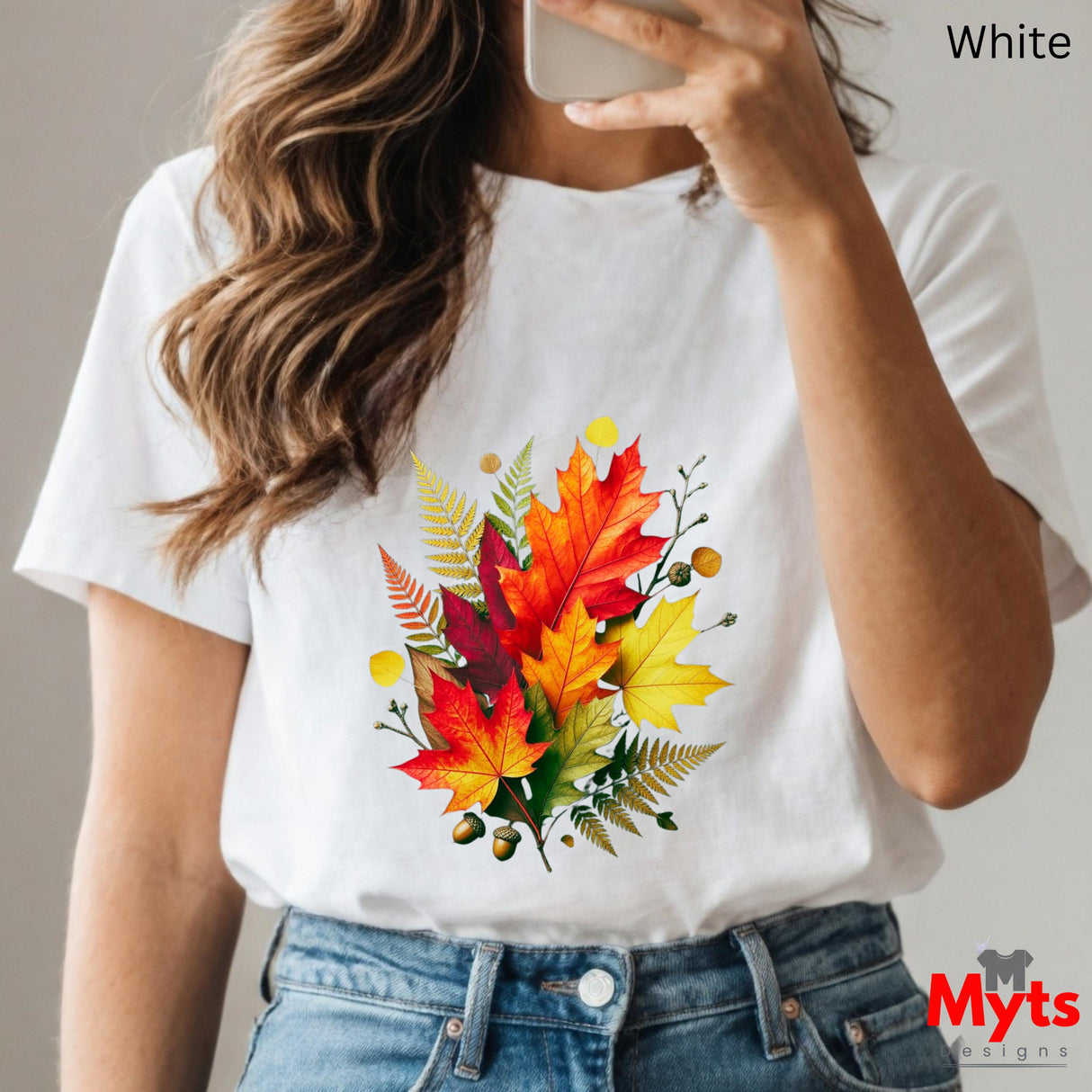 Person wearing a white t-shirt with autumn leaf design, holding a phone.