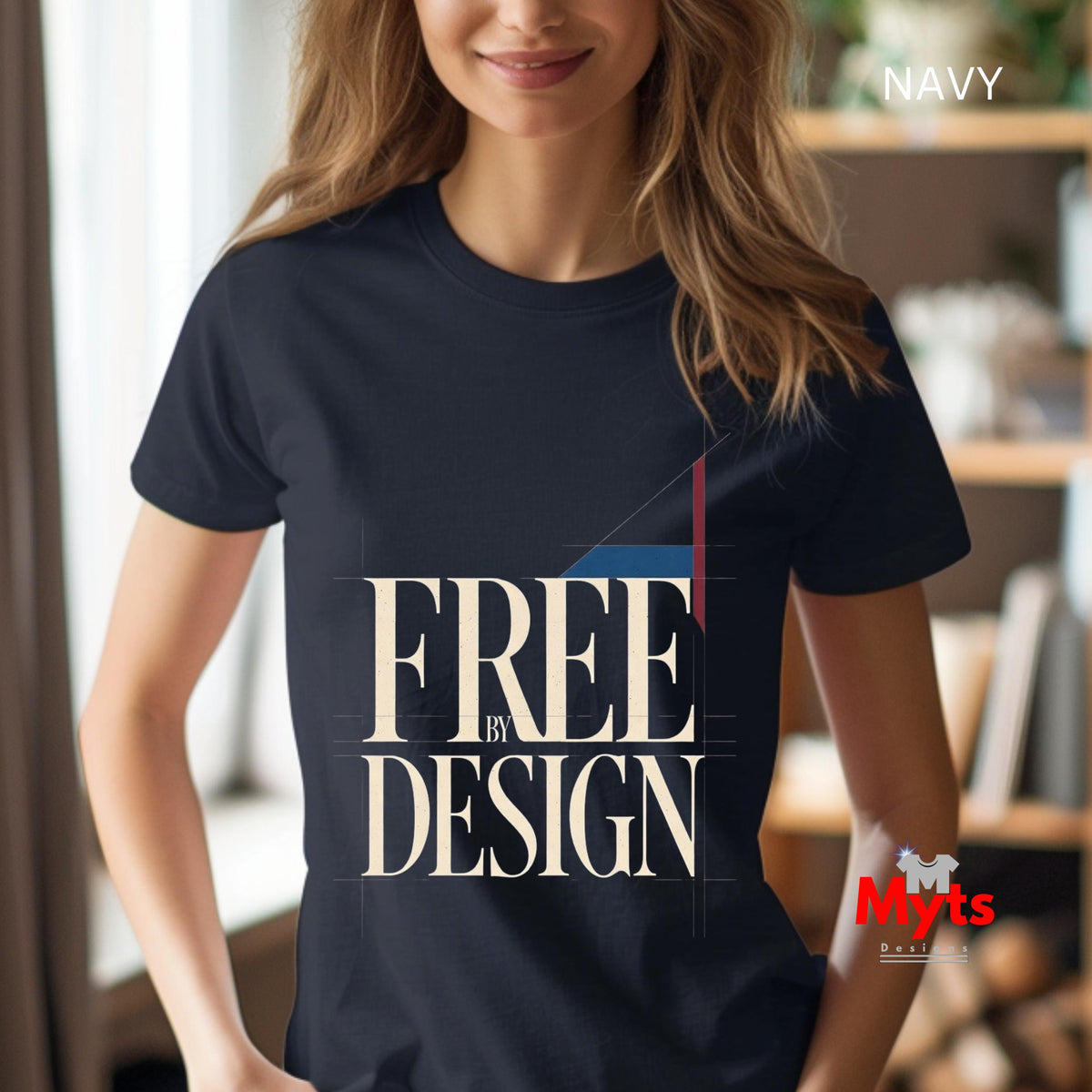 A woman wearing a navy blue graphic t-shirt with the text 'FREE BY DESIGN' in cream, set against a blurred indoor background. A 'NAVY' label is visible in the top right, and a 'Myts' brand logo is in the bottom right corner.