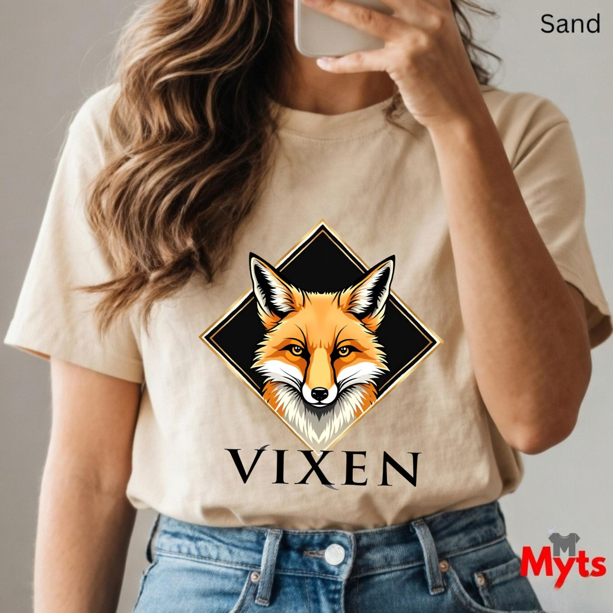 Person wearing a Sand t-shirt with a fox graphic and 'VIXEN' text, holding a phone.