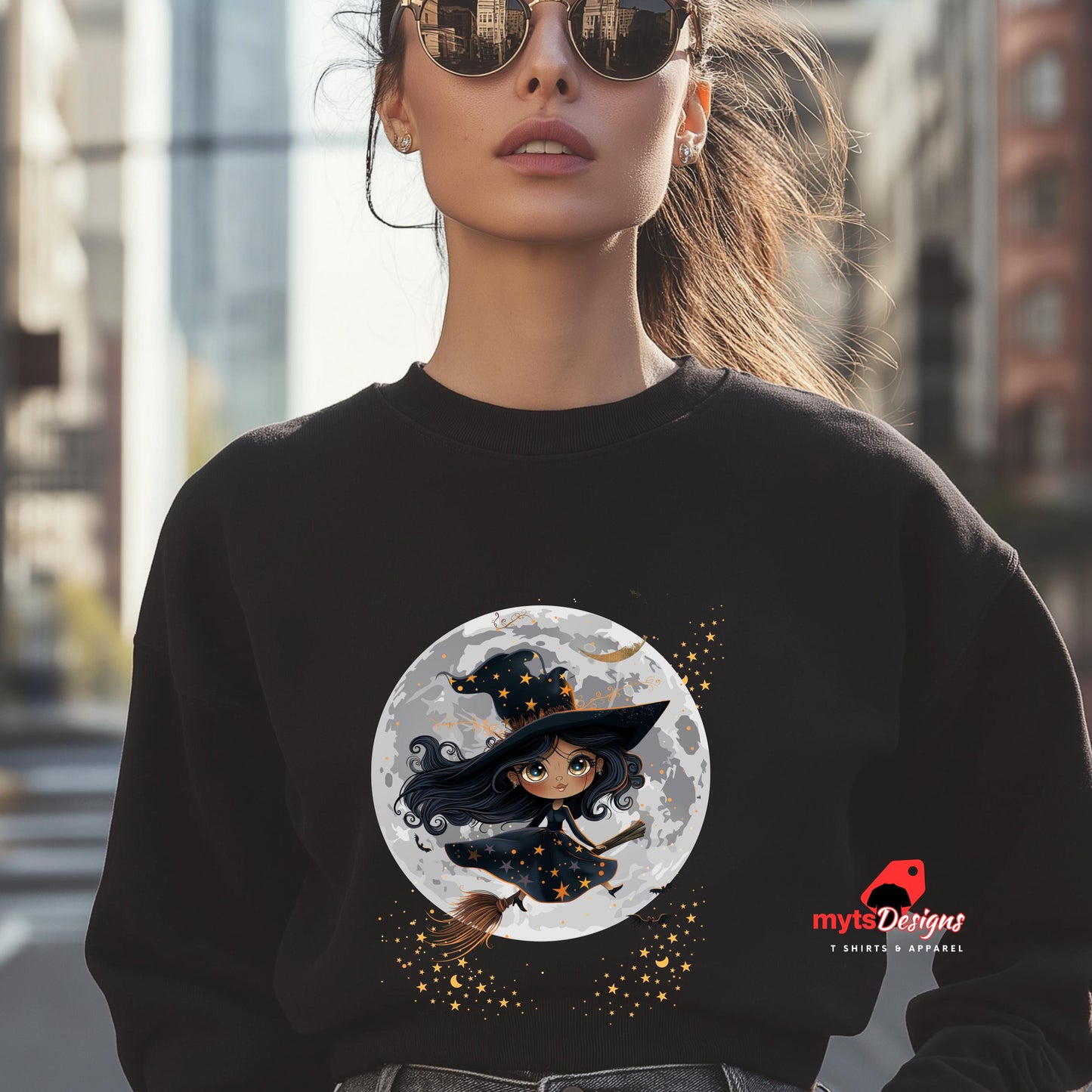 Person wearing a black sweatshirt with a witch design on a full moon, standing in an urban setting.