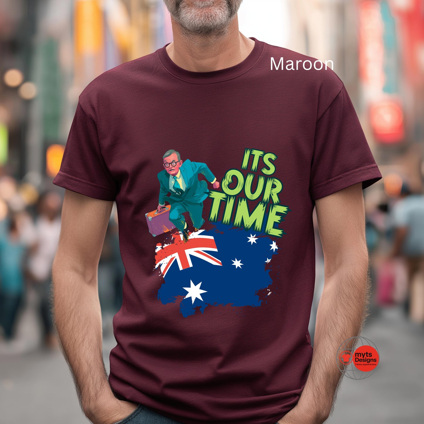 Man wearing a maroon t-shirt with a graphic design and text, standing in a blurred city street.