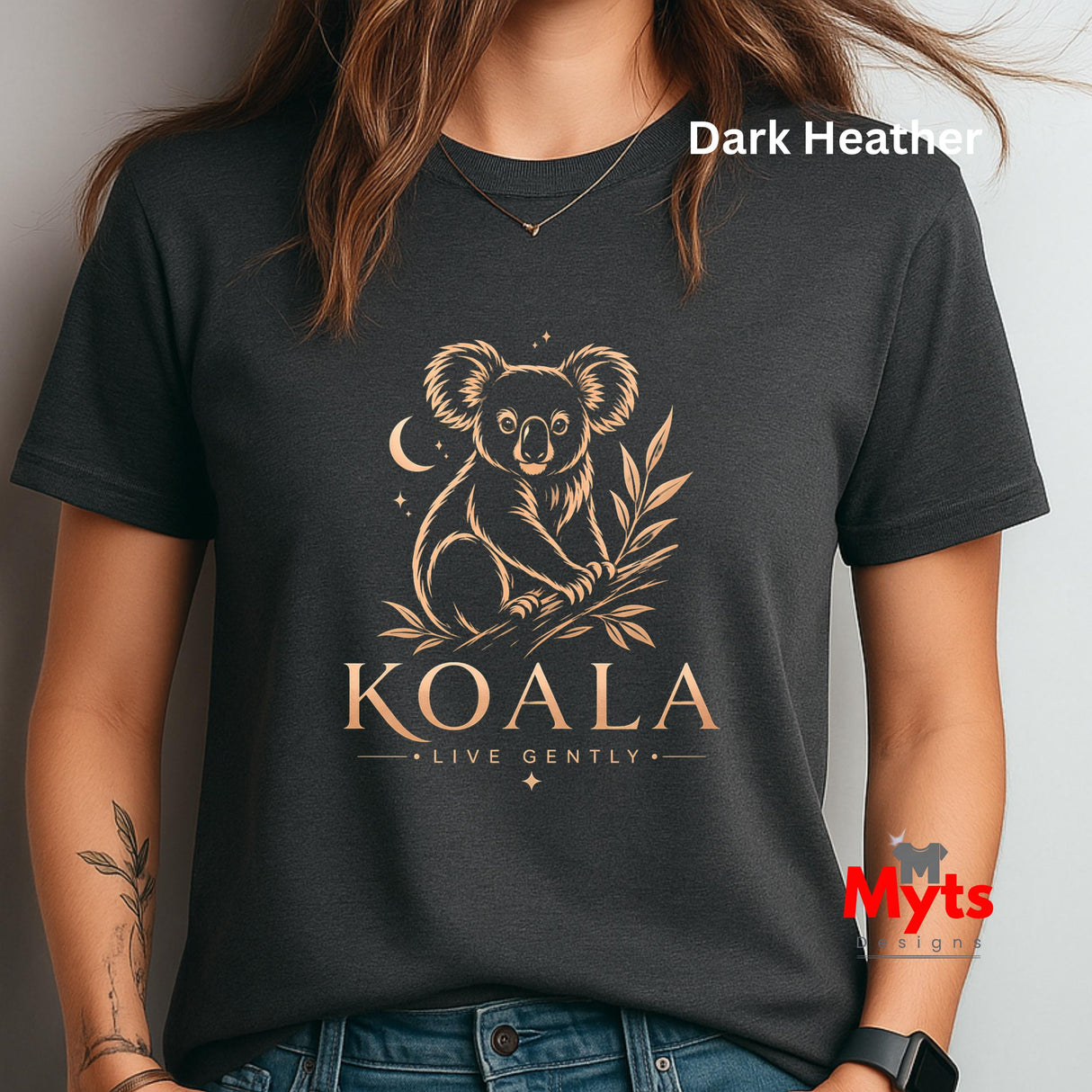 A woman wearing a dark heather charcoal t-shirt with a gold koala graphic and the text 'KOALA LIVE GENTLY' on the front. The image has a watermark 'Myts signs' in the bottom right corner.