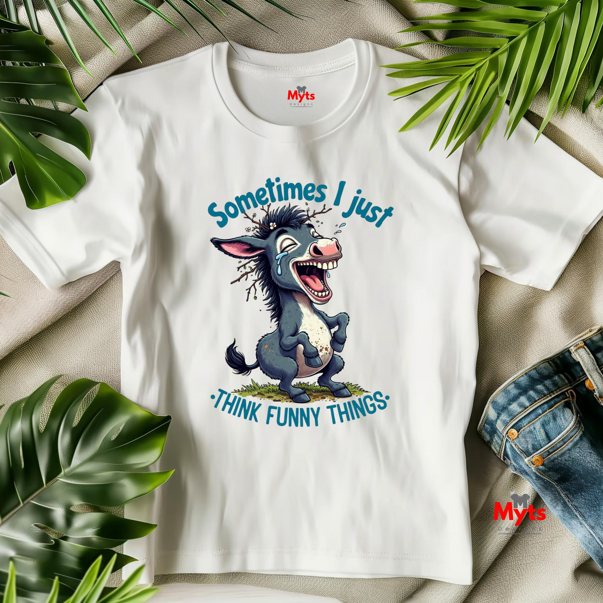 White t-shirt with cartoon donkey graphic and text 'Sometimes I just think funny things' on a beige surface with green leaves.