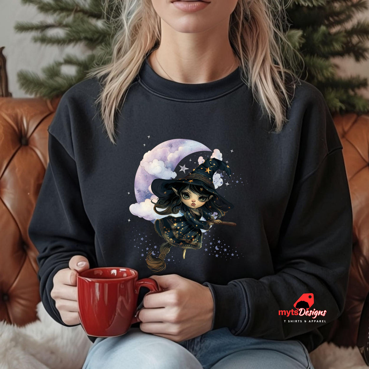Person wearing a black sweatshirt with a witch design, holding a red mug, sitting on a brown leather couch.