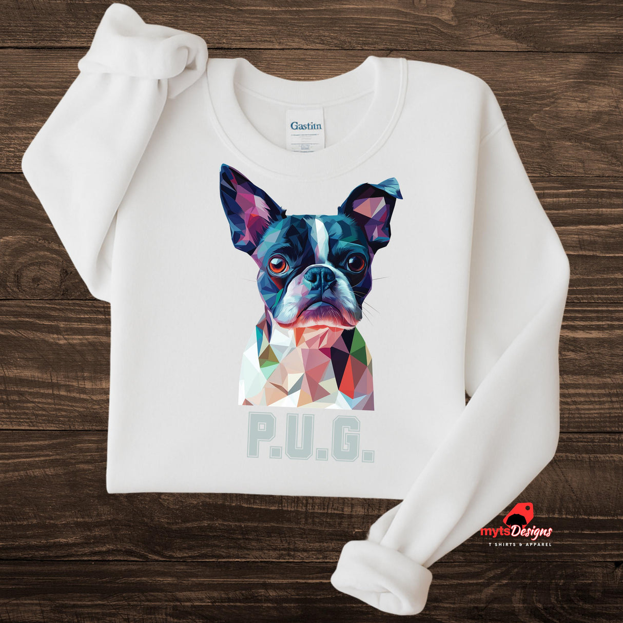 A white sweatshirt displayed on a wooden surface featuring a vibrant polygon-style dog portrait with the text “P.U.G.” below, designed by MytsDesigns