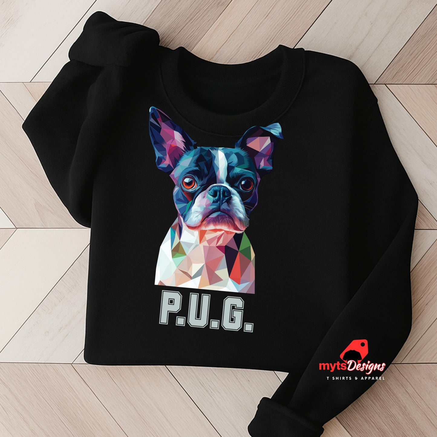 A black sweatshirt displayed on a wooden surface featuring a vibrant polygon-style dog portrait with the text “P.U.G.” below, designed by MytsDesigns