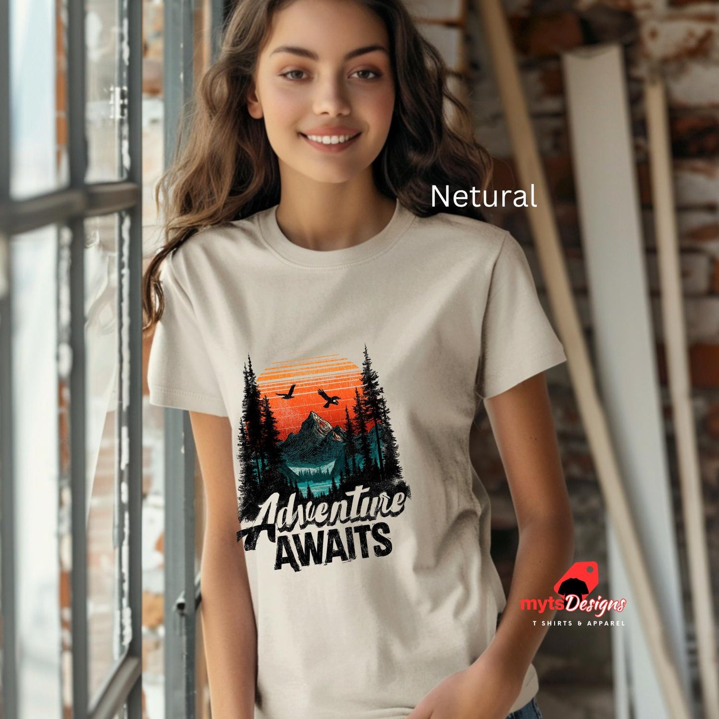 Woman wearing a t-shirt with a nature graphic and 'Adventure Awaits' text, standing indoors.