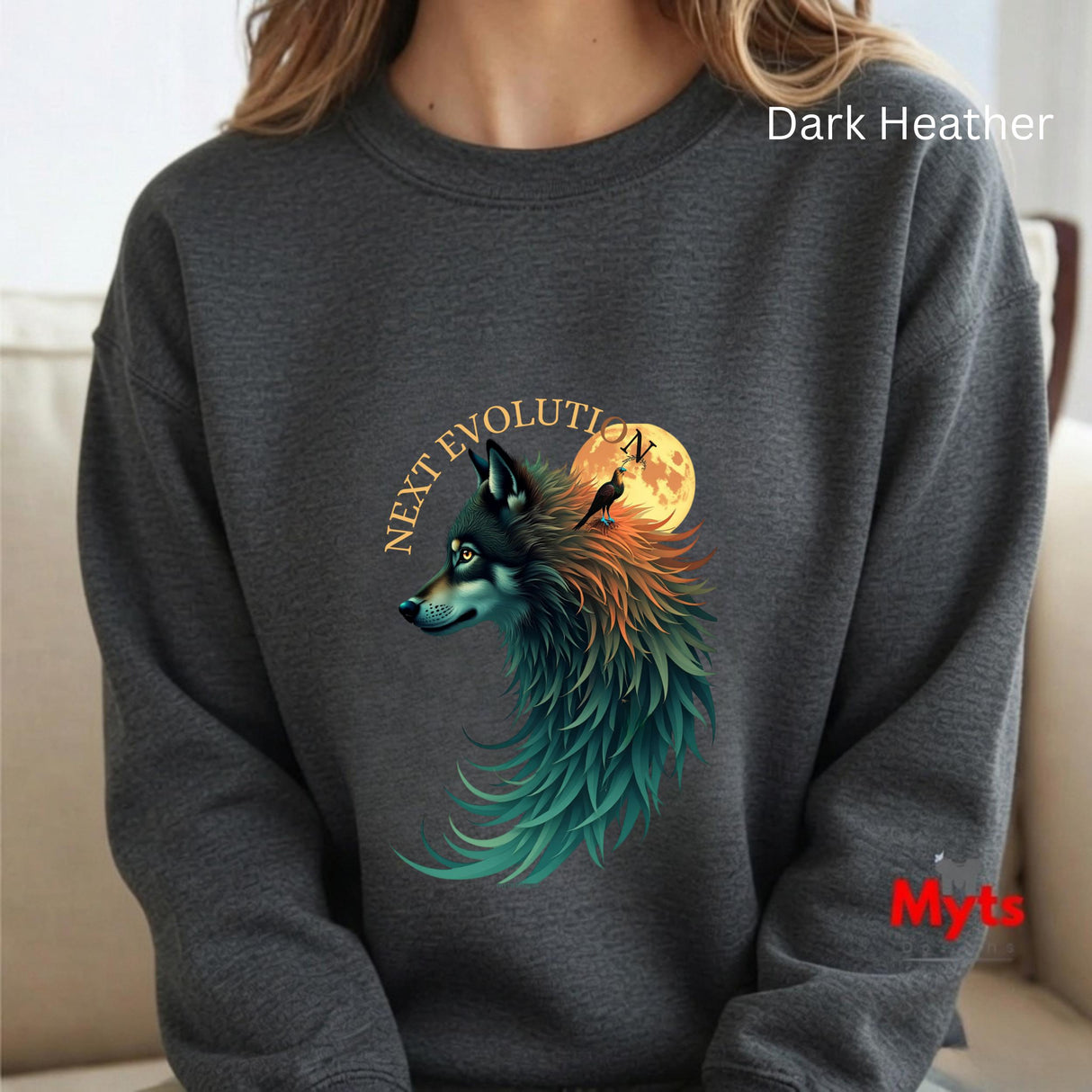 A person wearing a dark heather gray crewneck sweatshirt with a graphic of a wolf with teal, orange, and black feathers in front of a full moon, with the text 'NEXT EVOLUTION' above it. The sweatshirt has 'Dark Heather' text in white in the top right and a red 'Myts' logo in the bottom right.