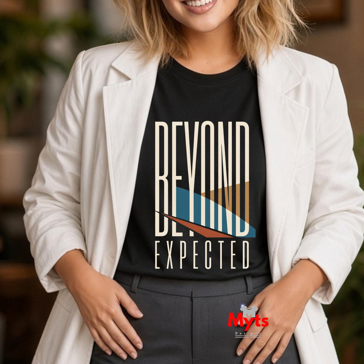 A woman wearing a black graphic T-shirt with the words 'BEYOND EXPECTED' in white, layered over a geometric blue, beige, and brown design, styled with a white blazer and dark gray pants.