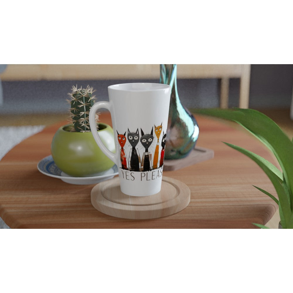 A white ceramic latte mug with a colorful illustration of four cats and the text 'CATS PLEASE' sitting on a round wooden coaster on a wooden table, styled with a small potted cactus and a green leaf in the background.