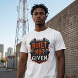 Person wearing a white t-shirt with 'Built Not Given' graphic design outdoors.