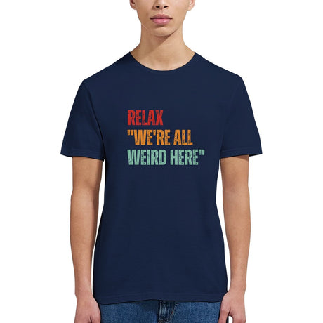 A woman wearing a navy retro-style casual tee featuring bold distressed vintage typography reading “Relax — We’re All Weird Here,” printed on ultra-soft Gildan 64000 cotton.