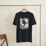 Black t-shirt with a graphic design of a person with a surfboard and 'Plashing Waves' text, hanging on a wooden rack.