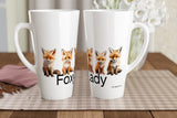 Two white ceramic mugs with printed fox illustrations and partial text, displayed on a checkered placemat on a wooden table with a blurred indoor background.