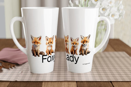 Two white ceramic mugs with printed fox illustrations and partial text, displayed on a checkered placemat on a wooden table with a blurred indoor background.