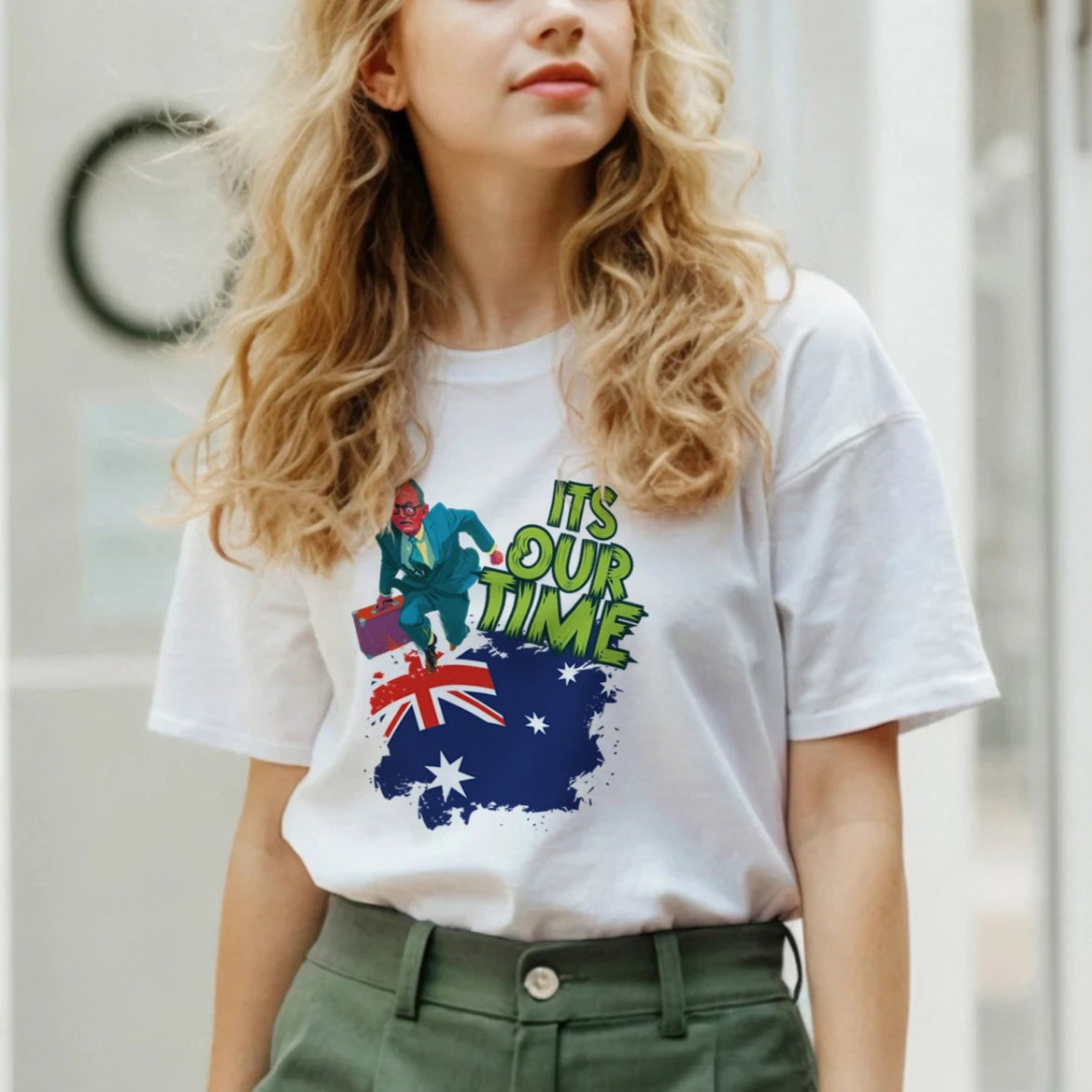 Woman wearing a white t-shirt with a colorful design and text, standing in front of a glass door.
