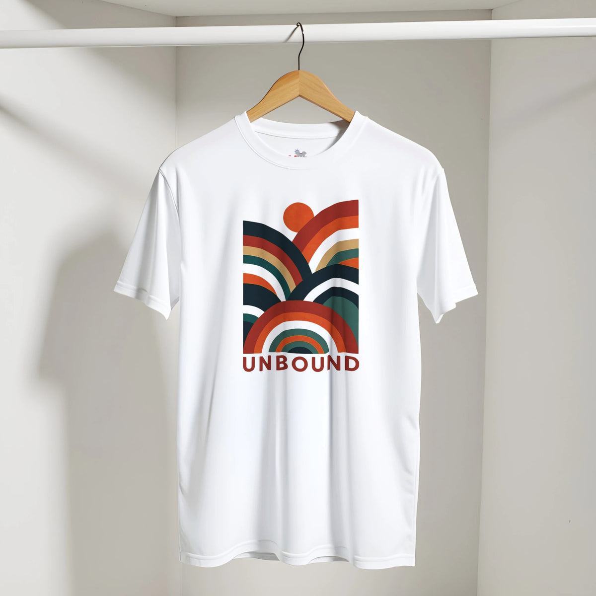 A white short-sleeve t-shirt hanging on a wooden hanger against a light gray wall. The shirt features a retro-style multicolor rainbow graphic on the chest with the word 'UNBOUND' printed in red underneath.