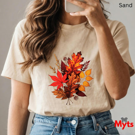 Person wearing a beige t-shirt with autumn leaf design, holding a phone.