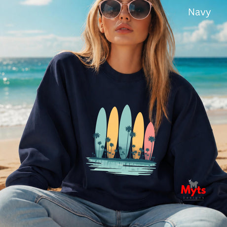 Woman wearing a navy sweatshirt with surfboard design sitting on a beach.