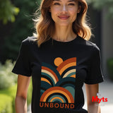 A woman wearing a black short-sleeve t-shirt with a retro 1970s-style multicolor graphic of arches and a sun, with the word 'UNBOUND' printed below it. The background is a blurred outdoor green setting.