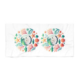 A white rectangular towel featuring two identical circular underwater-themed prints with seashells, starfish, coral, and sea plants in green, orange, and blue.