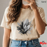 Person wearing a beige t-shirt with leaf design, holding a phone, on a plain background.