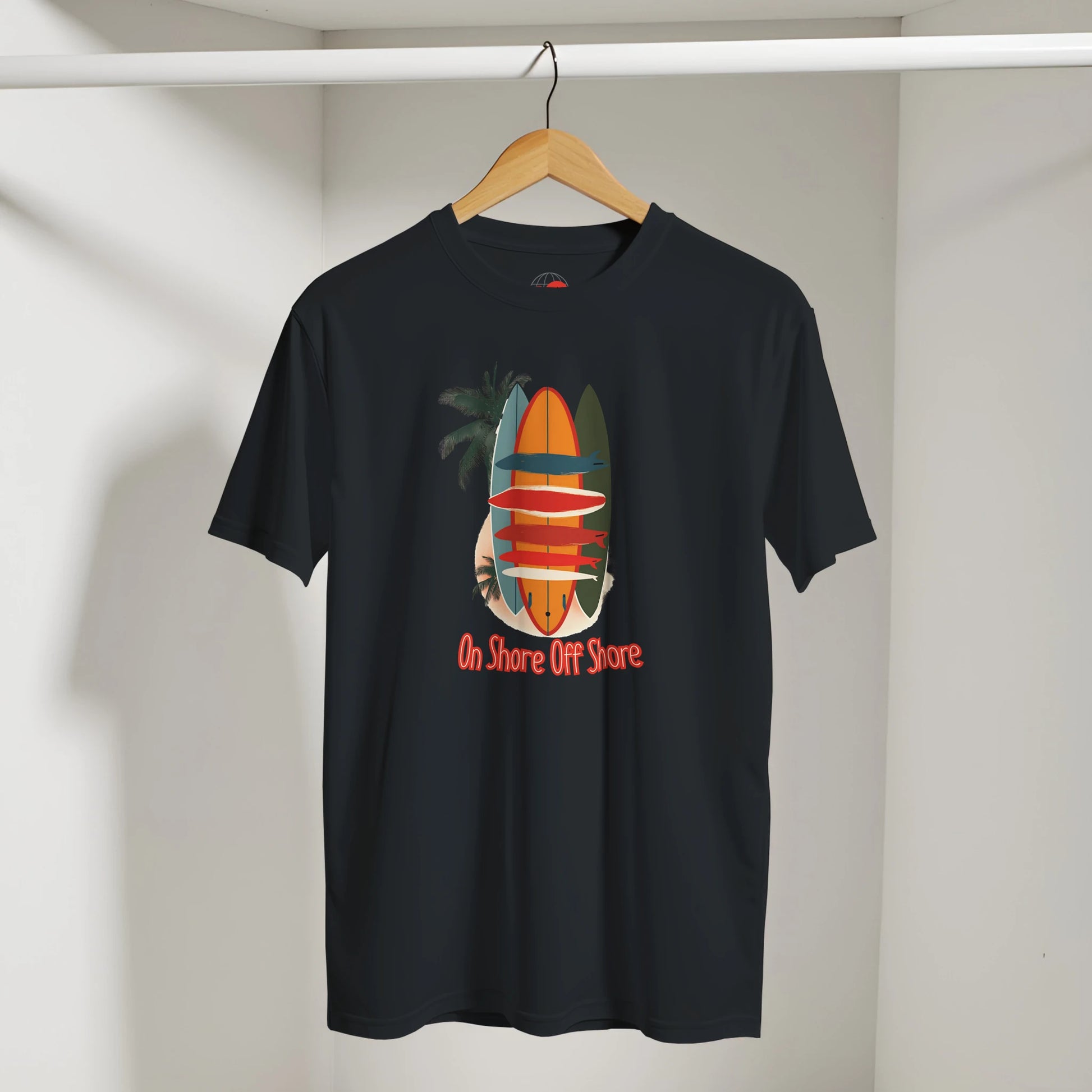 Black t-shirt with a colorful surfboard design and text on a hanger against a white wall.