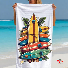 Person holding a beach towel with colorful surfboard design and ocean in the background