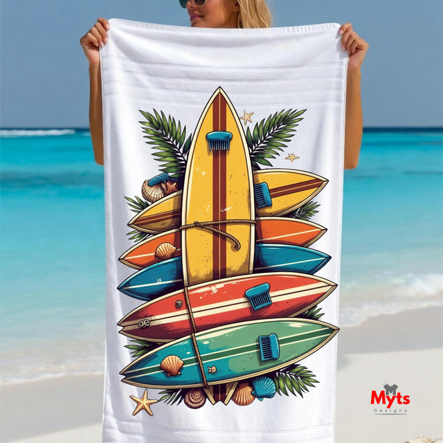 Person holding a beach towel with colorful surfboard design and ocean in the background