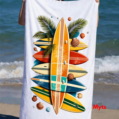 Beach towel with surfboard and palm tree design held by a person at the beach.