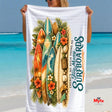 Towel with surfboard design and text held by a person on a beach
