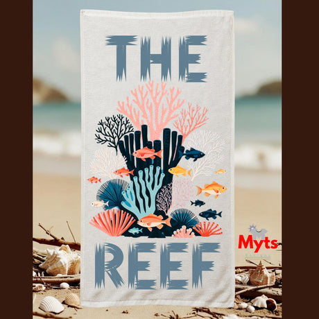 A rectangular beach towel with an ocean-themed graphic print featuring the text 'THE REEF' and colorful coral, fish, and shell illustrations, shown hanging against a blurred beach background. A red 'Myts' logo appears on the lower right.