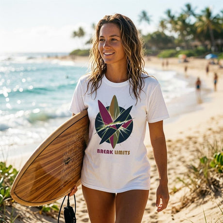 Woman on a beach holding a wooden surfboard, wearing a white t-shirt with a colorful graphic and text.