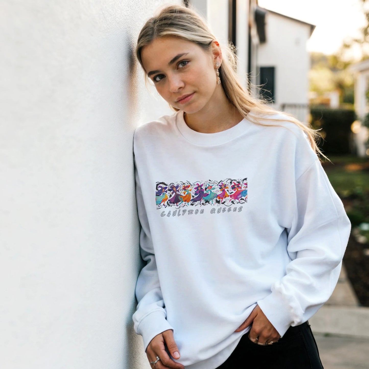 Woman wearing a white sweatshirt with colorful graphics and text, standing against a light-colored wall.