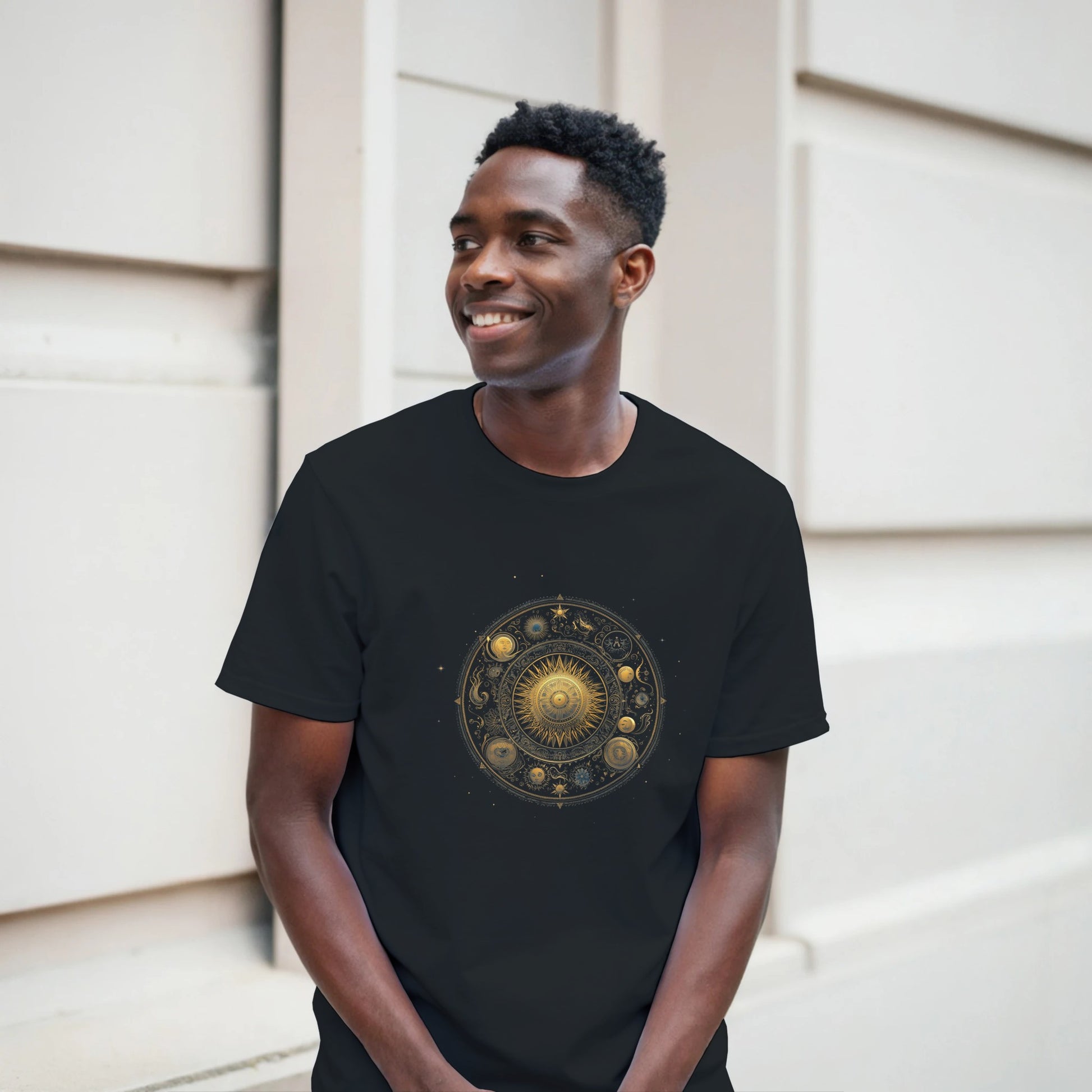 Man wearing a black t-shirt with a gold and bronze circular design, standing against a neutral background.