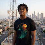 A man wearing a black graphic t-shirt with a colorful wolf and moon design, standing in front of a city skyline at sunset.