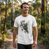 A man standing on a forest path wearing a white crew-neck t-shirt with a detailed black and gray graphic of a koala on a tree branch.