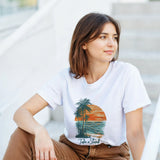 Woman wearing a white t-shirt with a palm tree design and text, sitting on steps.