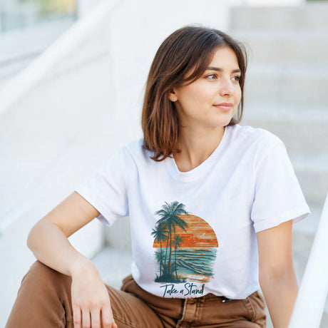 Woman wearing a white t-shirt with a palm tree design and text, sitting on steps.