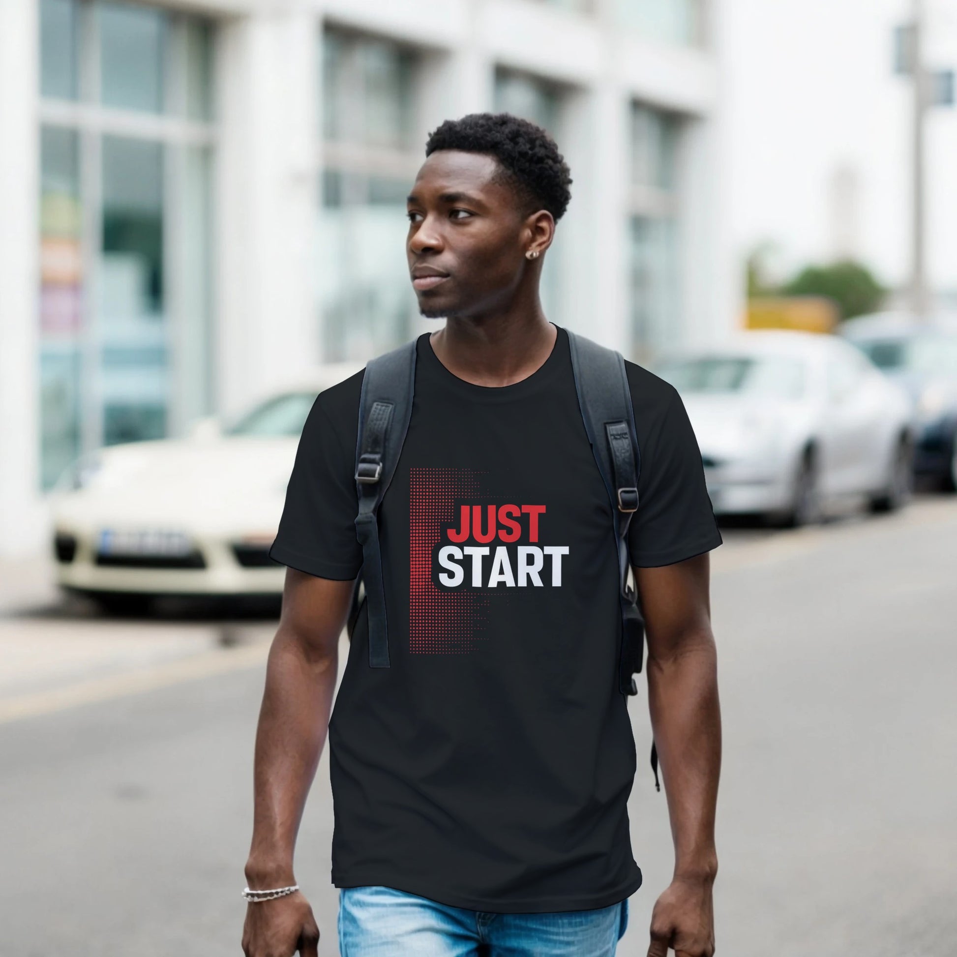 Man wearing a black t-shirt with 'JUST START' text on a street.
