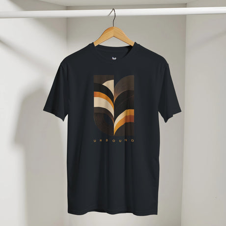 A black short-sleeve t-shirt hanging on a wooden hanger against a light gray wall. The shirt features a large graphic print on the front with abstract wavy stripes in brown, beige, and orange, with the word 'UNBOUND' printed below in gold.