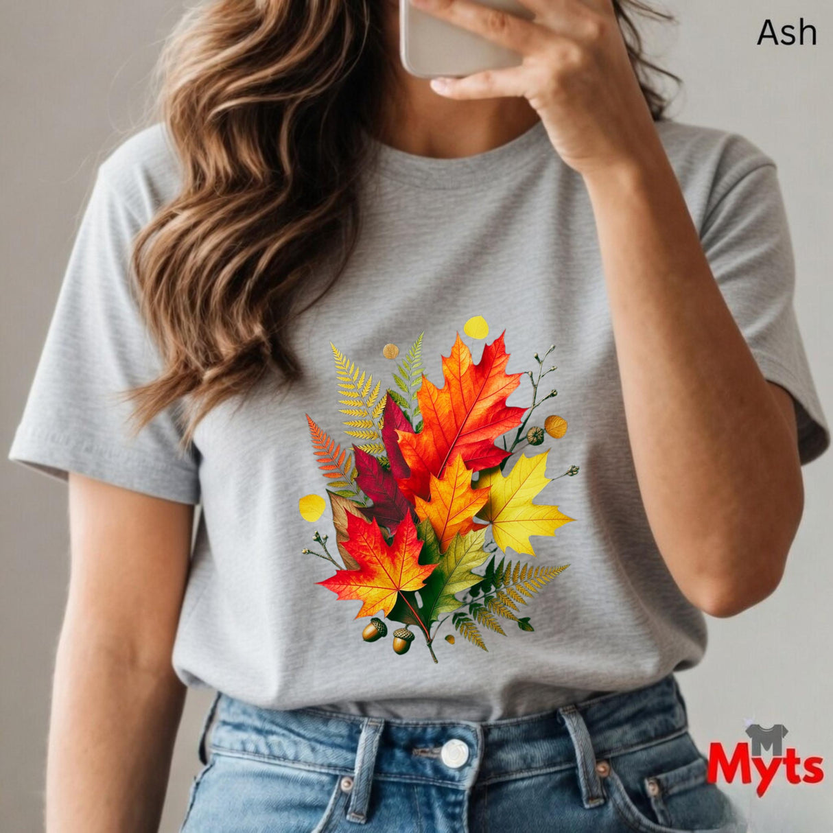Person wearing an Ash t-shirt with a colorful leaf design, holding a phone.