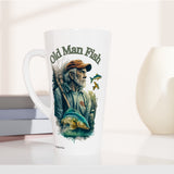 A tall white ceramic latte mug with a colorful 'Old Man Fish' illustration, styled on a white surface next to stacked books and two ceramic vases.