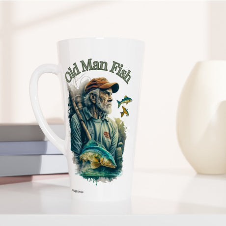 A tall white ceramic latte mug with a colorful 'Old Man Fish' illustration, styled on a white surface next to stacked books and two ceramic vases.