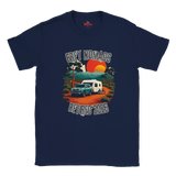 A navy blue short-sleeve t-shirt with a retro-style graphic on the front. The graphic features a teal pickup truck towing a white caravan on an orange dirt road, with a sunset in orange and yellow, trees, and the text 'GREY NOMADS RETIRED 2026'.