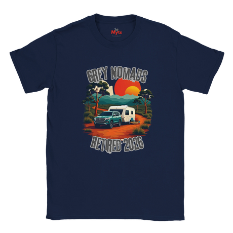 A navy blue short-sleeve t-shirt with a retro-style graphic on the front. The graphic features a teal pickup truck towing a white caravan on an orange dirt road, with a sunset in orange and yellow, trees, and the text 'GREY NOMADS RETIRED 2026'.