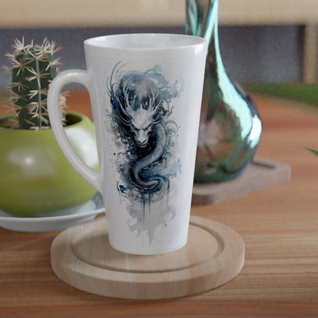 A tall white ceramic mug with a blue dragon illustration, resting on a round wooden coaster on a wooden table. A small green potted cactus and a metallic teal vase are visible in the background.