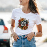 A woman wearing a white t-shirt with a floral design and text, standing outdoors.
